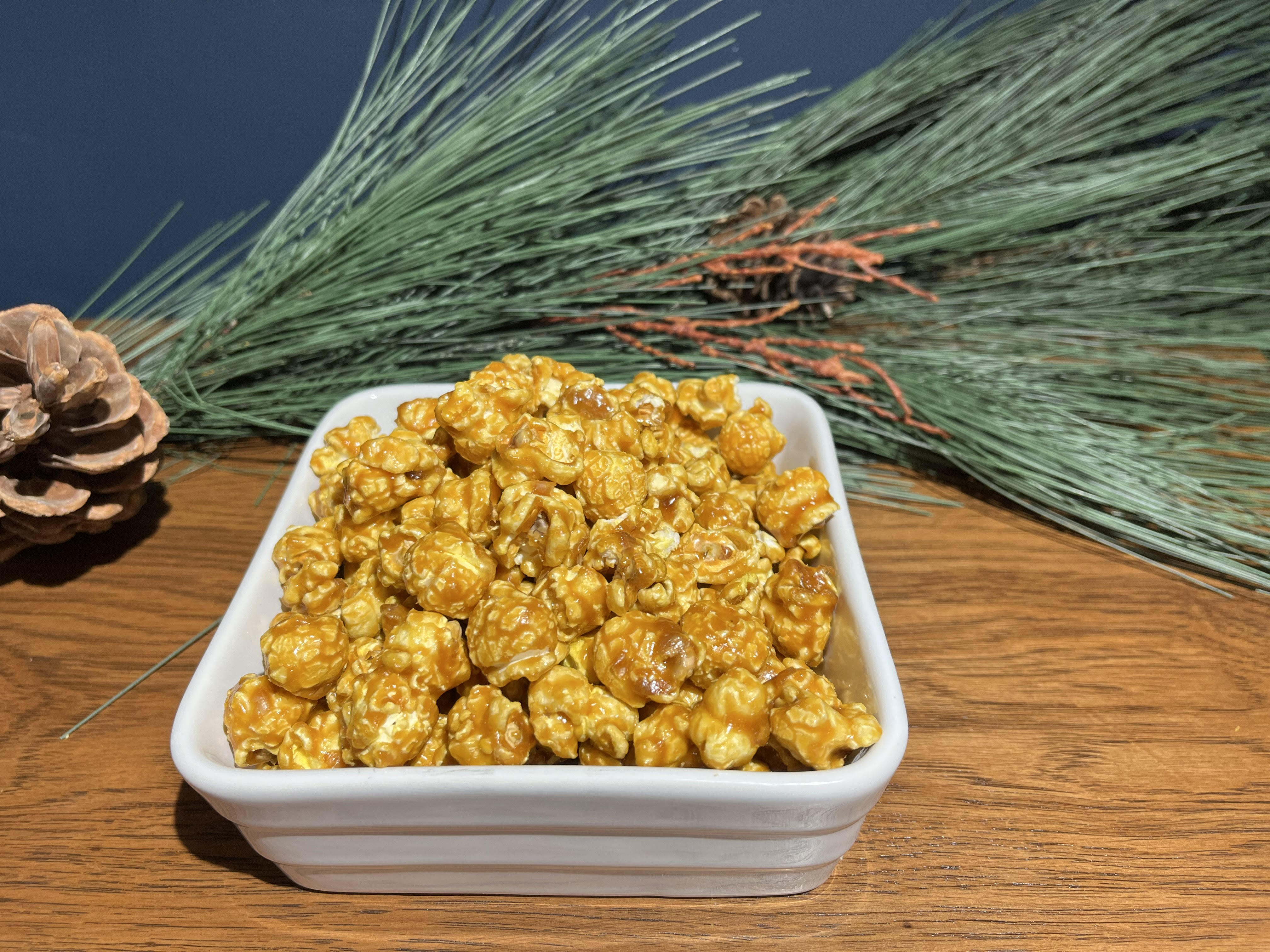 Photo of a square white dish filled with caramel popcorn. Green decor in background in front of dark blue wall