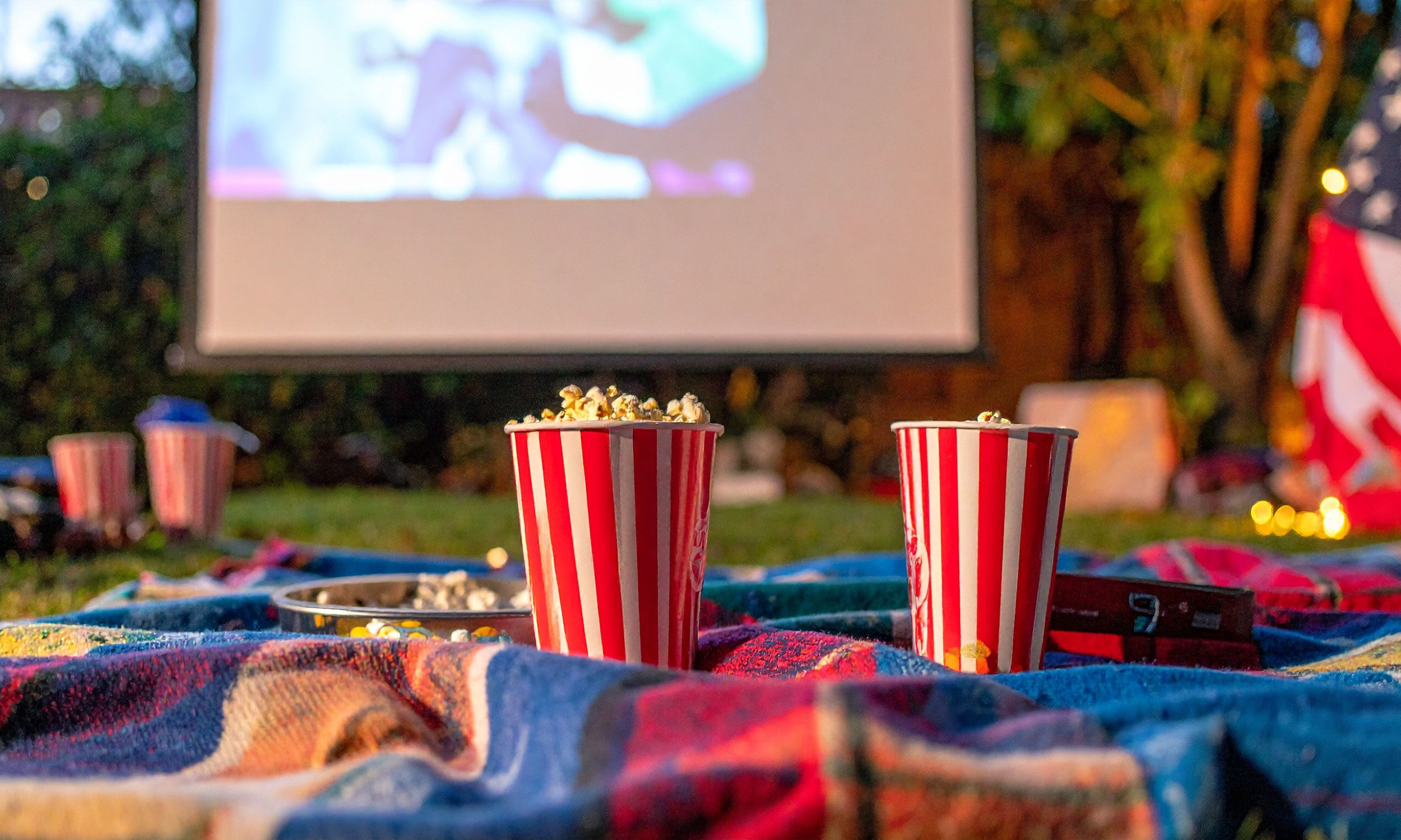 Cups of Bytown Gourmet Popcorn in paper cups placed on blanket in front of outdoor movie screen