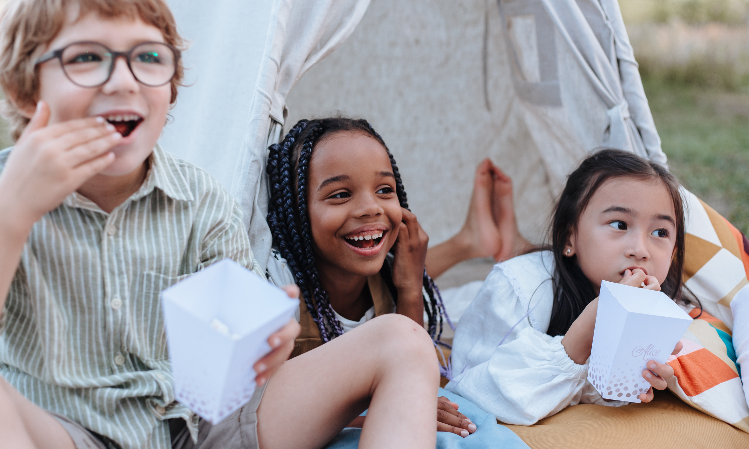 Three children sitting together with Bytown Gourmet popcorn, enjoying a movie night outdoors.